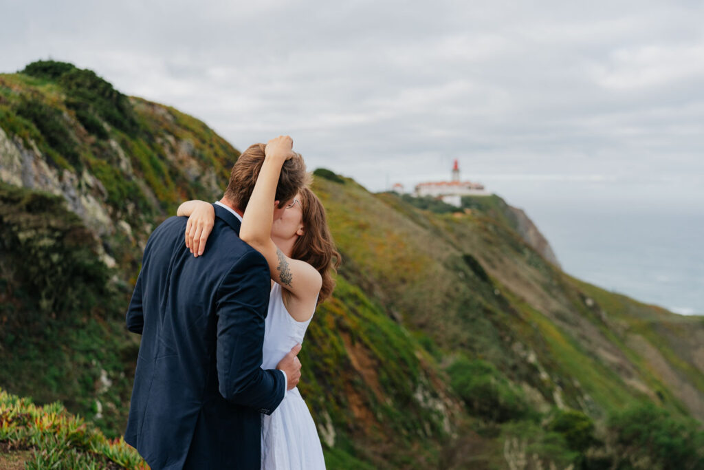 Zamilovaný pár ve svatebním se objímá na sytě zelených stráních nad portugalskou Praia da Ursa